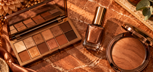 Flat lay of copper eyeshadow palette, copper nail polish, and bronzer arranged on a warm marble surface