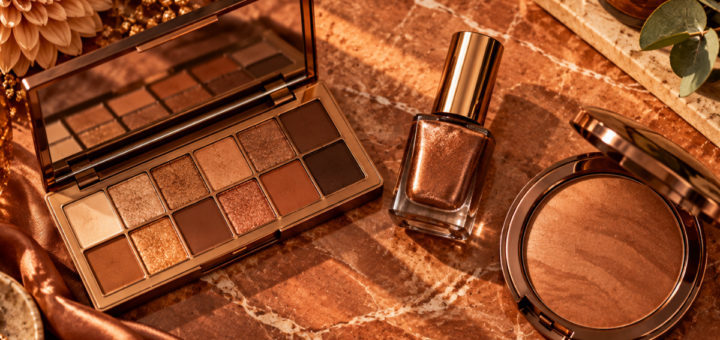 Flat lay of copper eyeshadow palette, copper nail polish, and bronzer arranged on a warm marble surface
